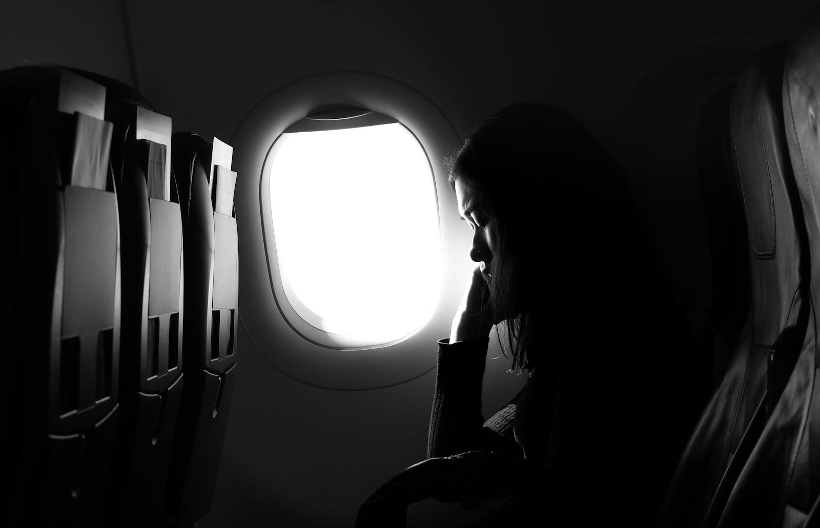 A woman in silhouette sits by an airplane window, experiencing travel journey.