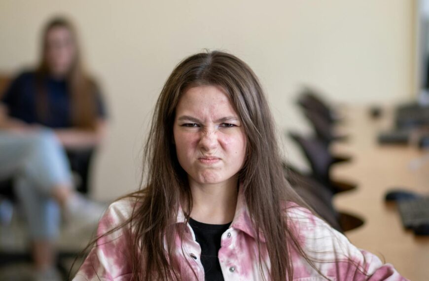 An angry teenage girl sitting in a classroom, displaying a frustrated expression.