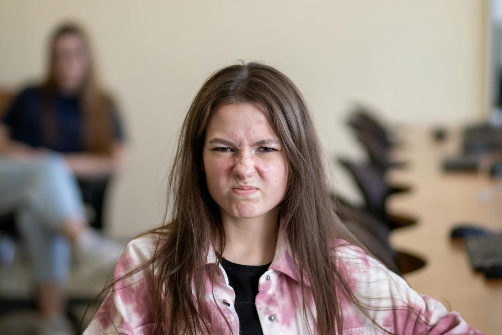 An angry teenage girl sitting in a classroom, displaying a frustrated expression.