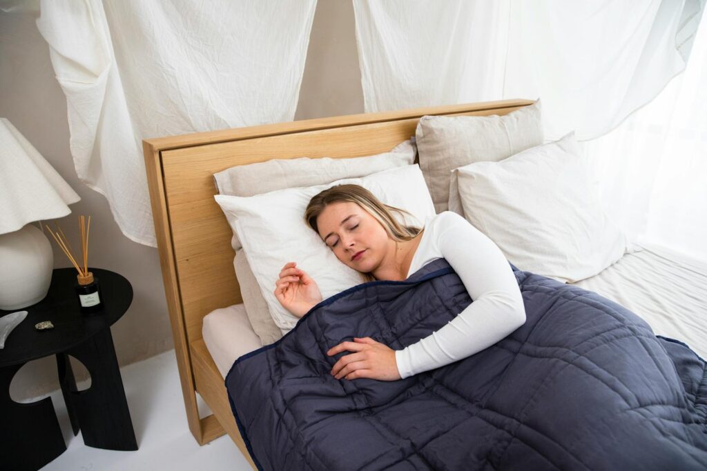 A serene scene of a woman resting with a weighted blanket in a light-filled cozy bedroom.