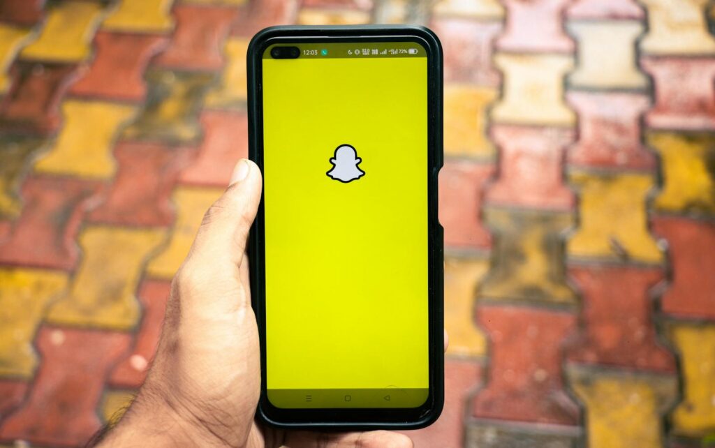 Snapchat app logo displayed on a smartphone against a vibrant outdoor patterned surface.