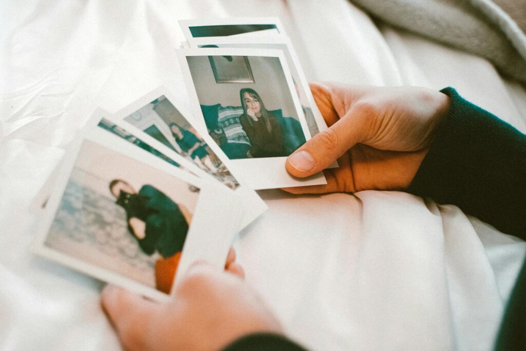 Hands gently holding a collection of printed photographs on a white bedspread.