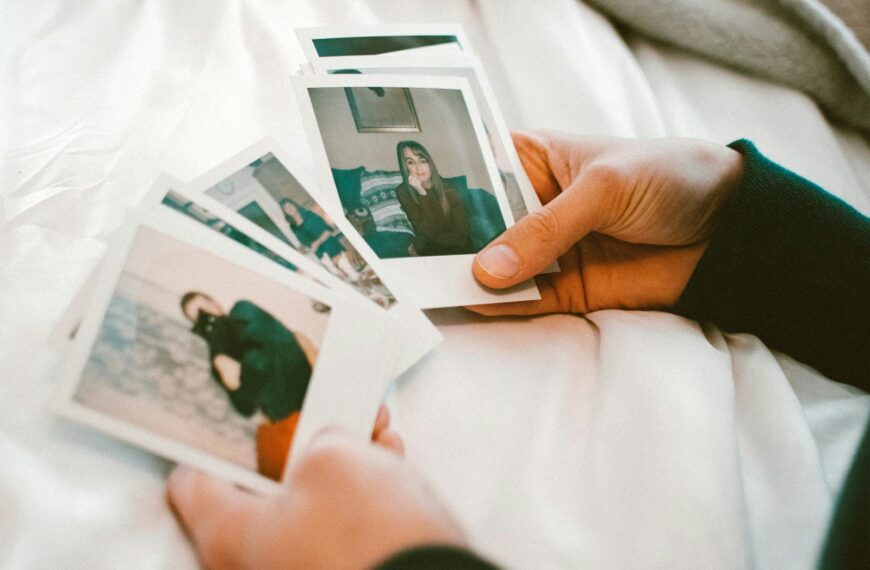 Hands gently holding a collection of printed photographs on a white bedspread.