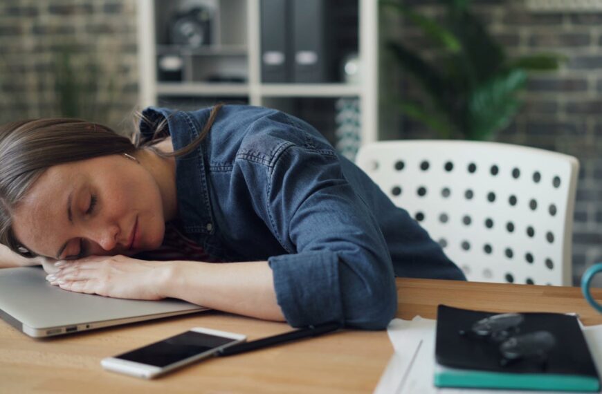 Tired woman resting her head on a laptop at an office desk, symbolizing workplace fatigue.