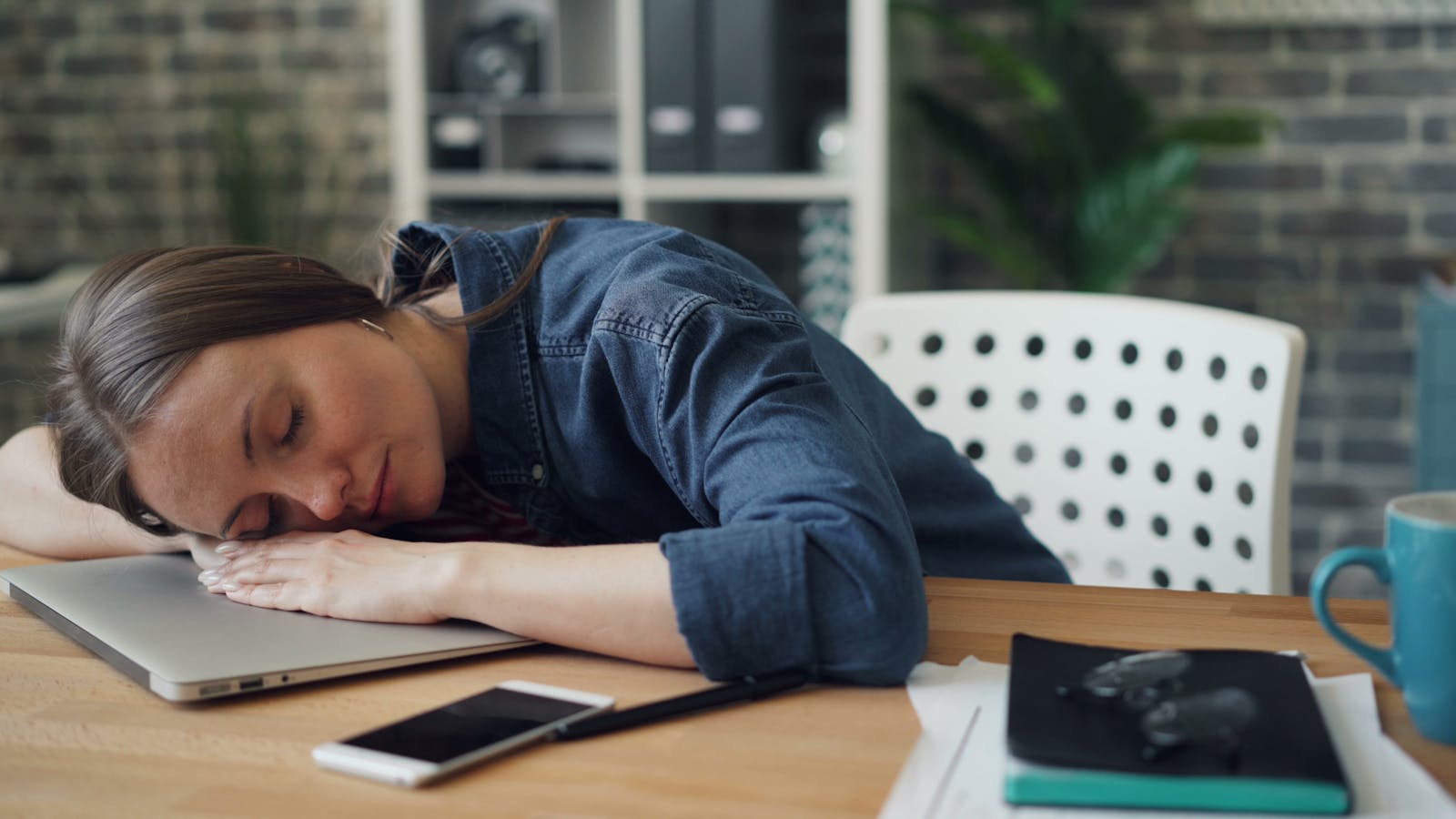 Tired woman resting her head on a laptop at an office desk, symbolizing workplace fatigue.