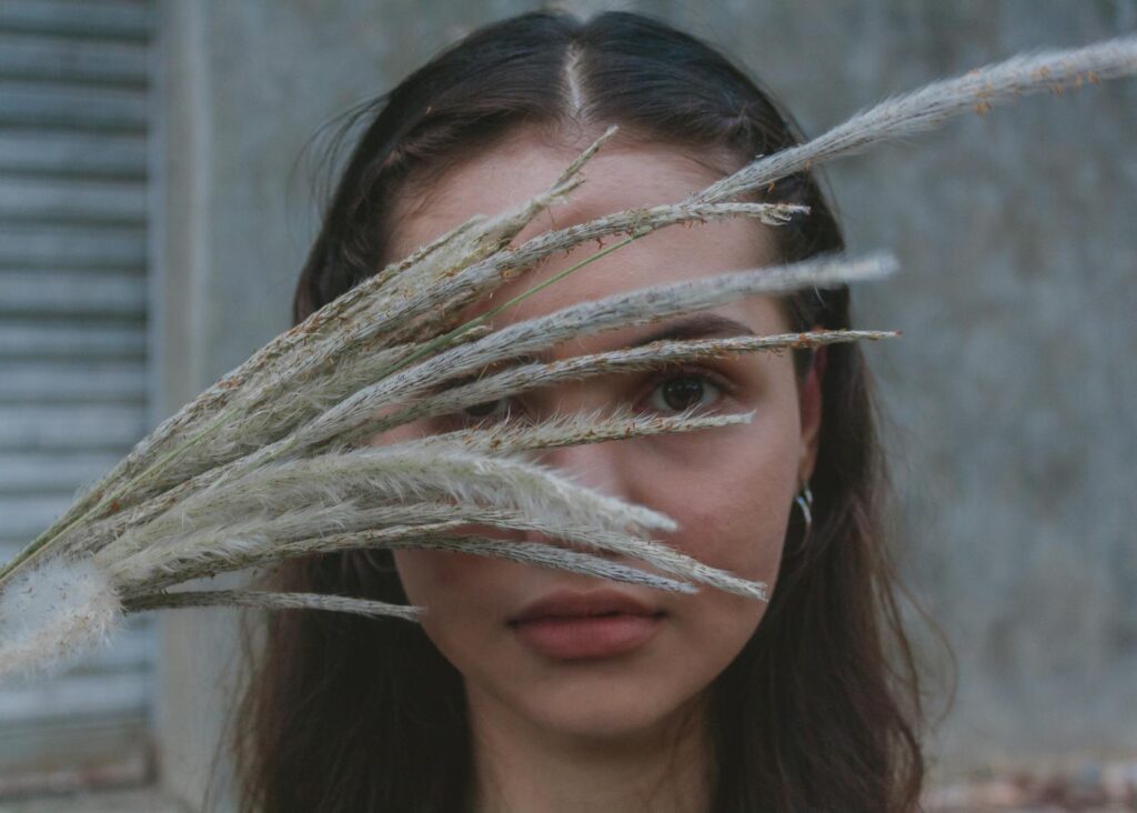 Artistic portrait of a woman with grass stalks obscuring her face, creating a mysterious and serene mood.