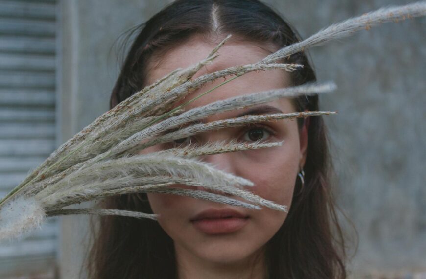 Artistic portrait of a woman with grass stalks obscuring her face, creating a mysterious and serene mood.
