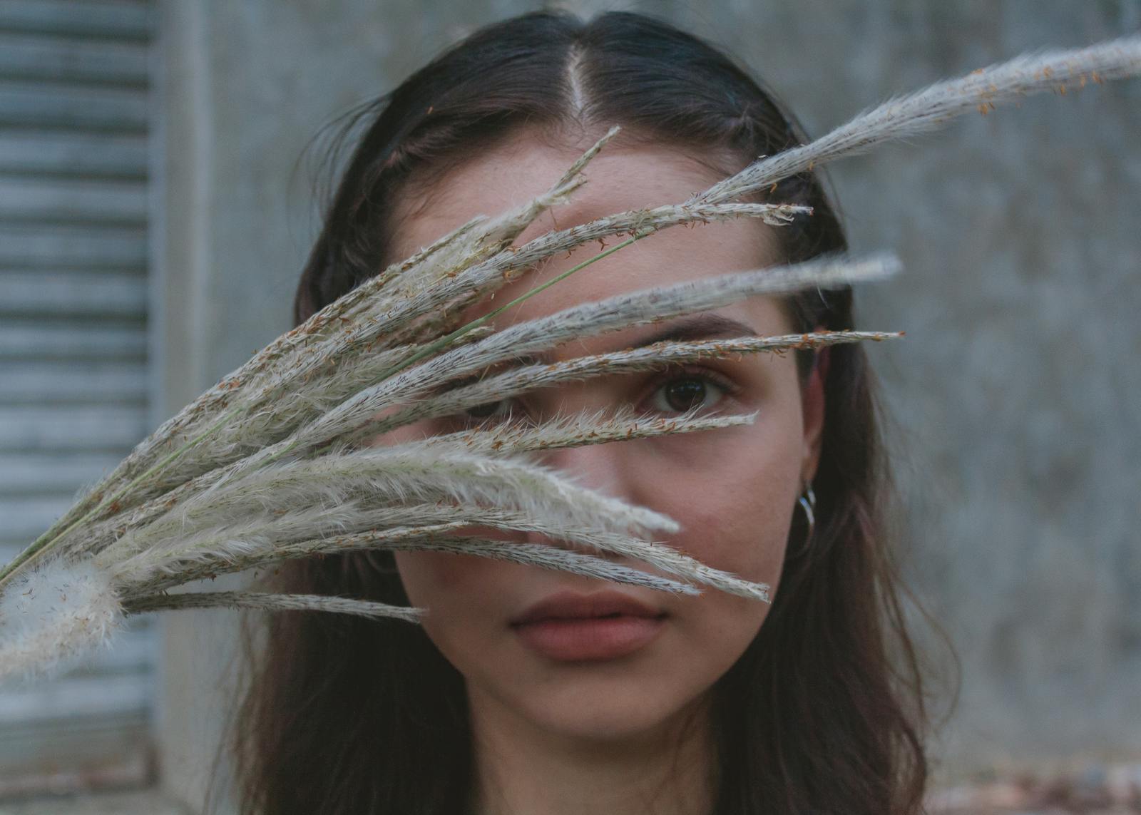 Artistic portrait of a woman with grass stalks obscuring her face, creating a mysterious and serene mood.