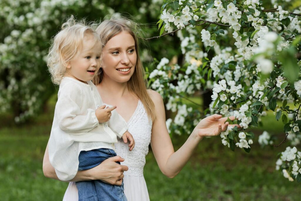 A mother with her young child in a lush orchard full of blooming white flowers, capturing a tender moment.