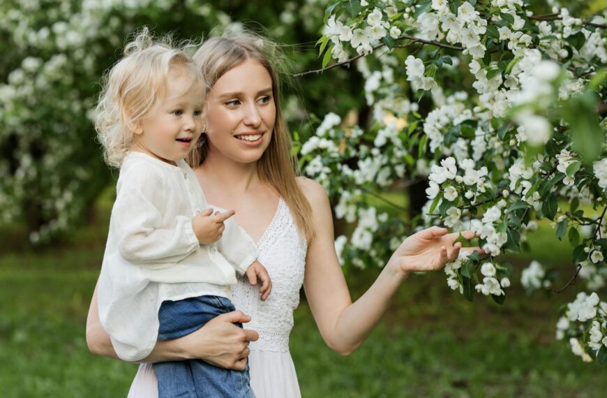 A mother with her young child in a lush orchard full of blooming white flowers, capturing a tender moment.
