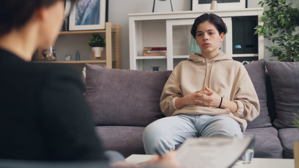Calm teenager sitting on a sofa during a therapy session with a professional therapist.