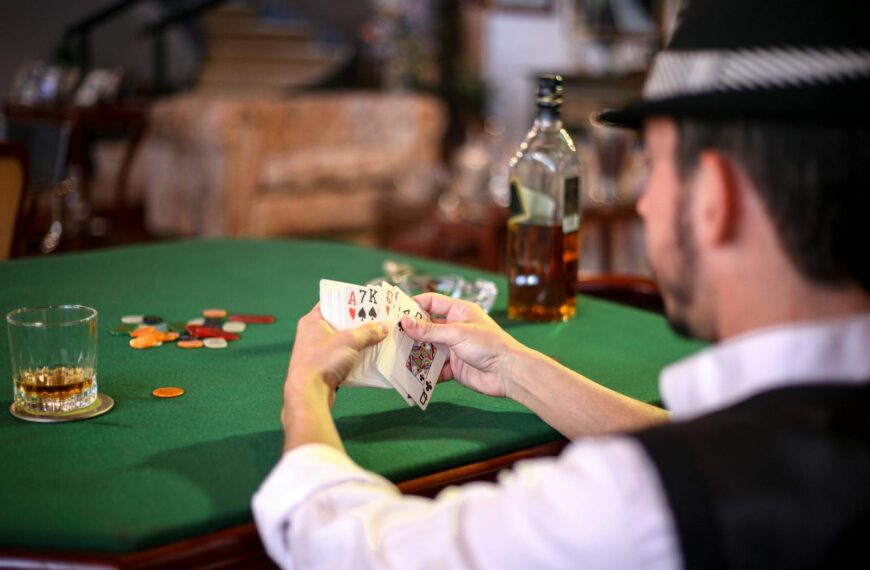 A man holding a poker hand at a casino table with chips and whiskey, conveying a gambling atmosphere.