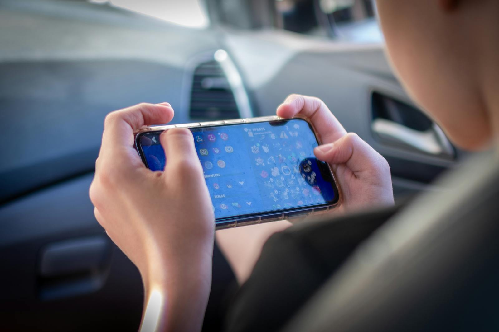 A teenager plays a mobile game while sitting inside a car, showcasing modern technology engagement.