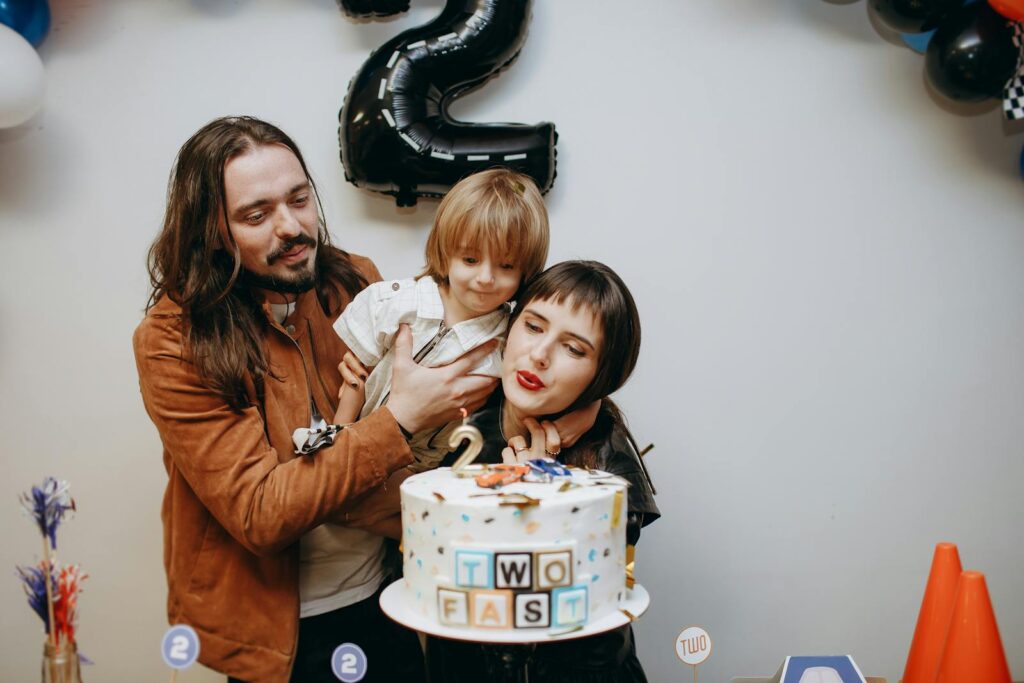 A joyful family celebrates their child's second birthday with a themed cake.