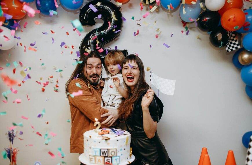 Cheerful family celebrating a child's second birthday with balloons, confetti, and cake.