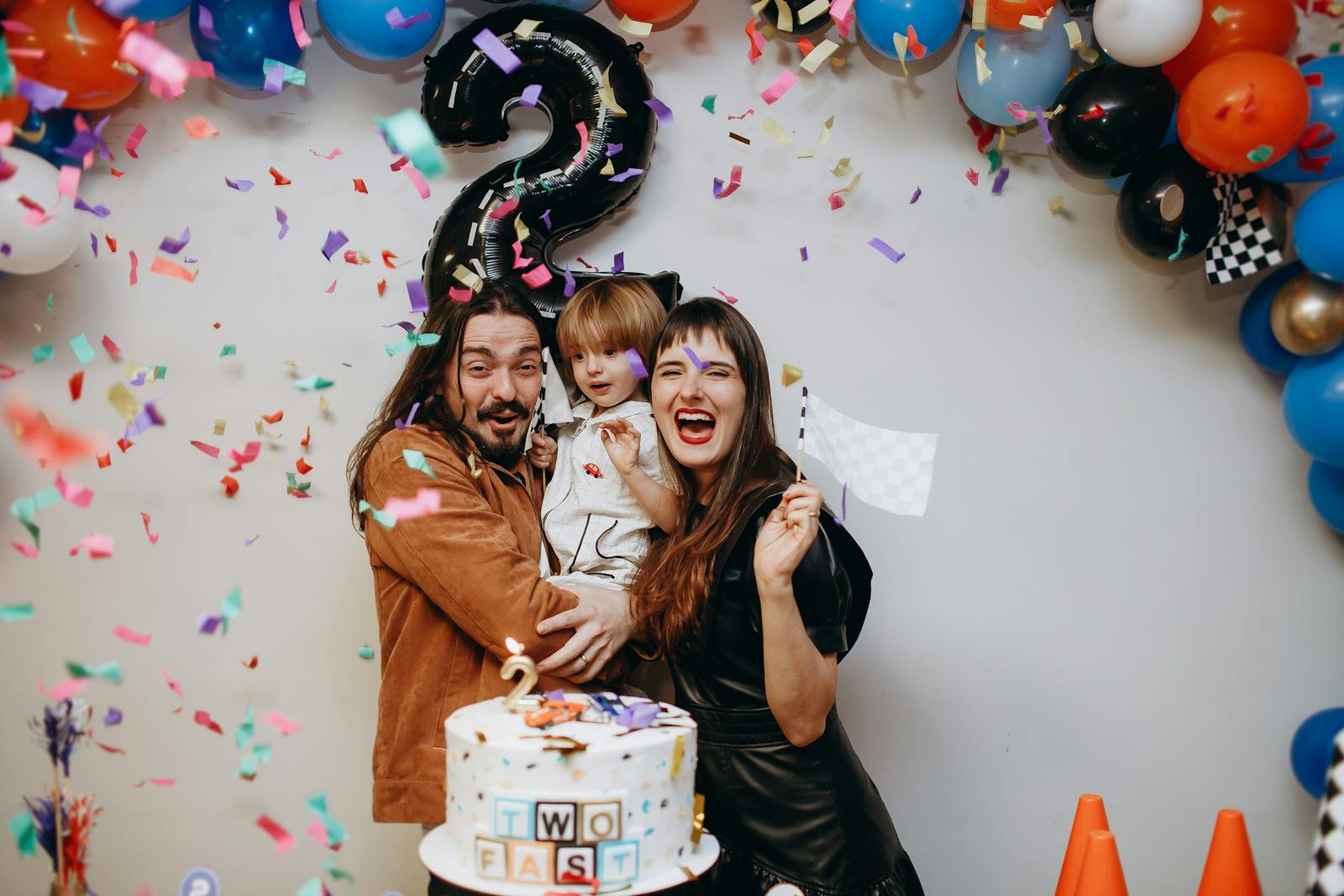 Cheerful family celebrating a child's second birthday with balloons, confetti, and cake.