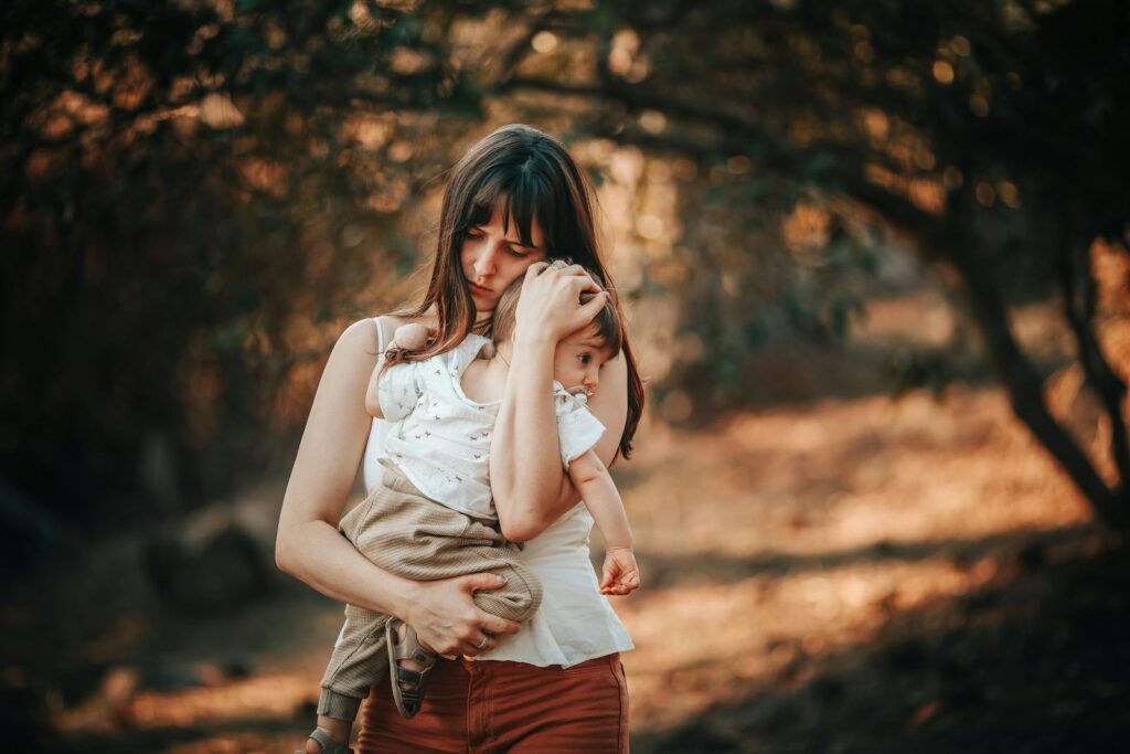 A serene portrait of a mother embracing her child in a warm outdoor setting.