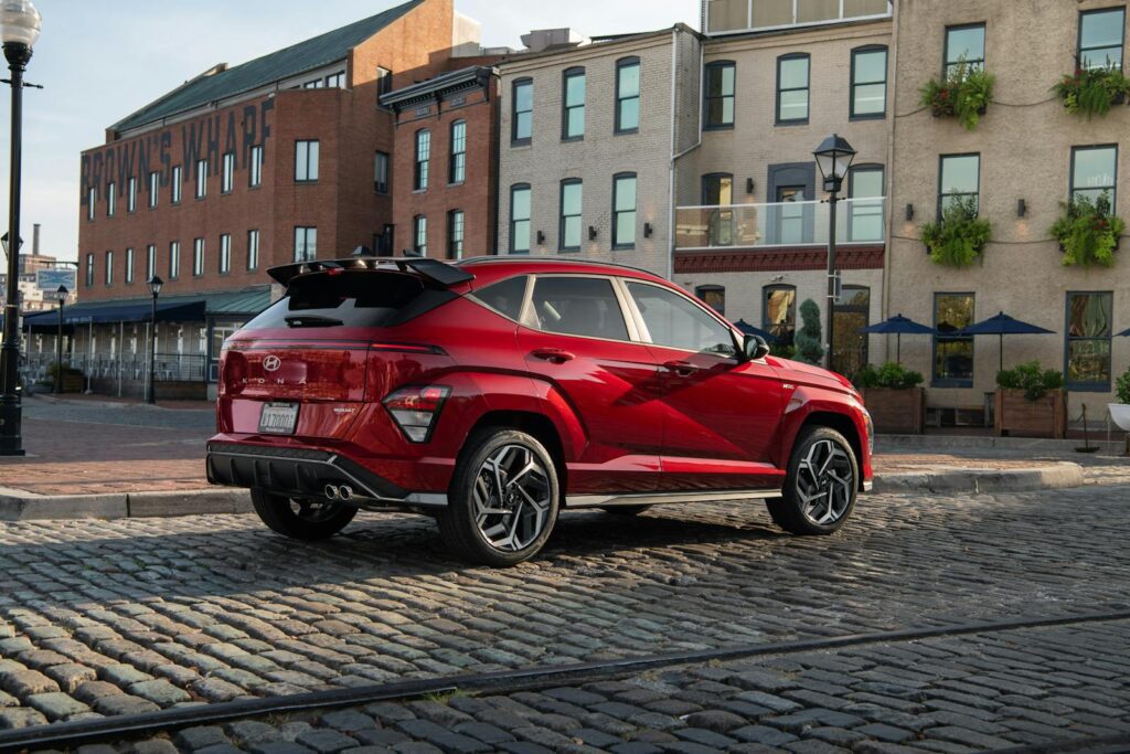 A sleek red Hyundai Kona SUV parked outdoors on a cobblestone street, near historic buildings.