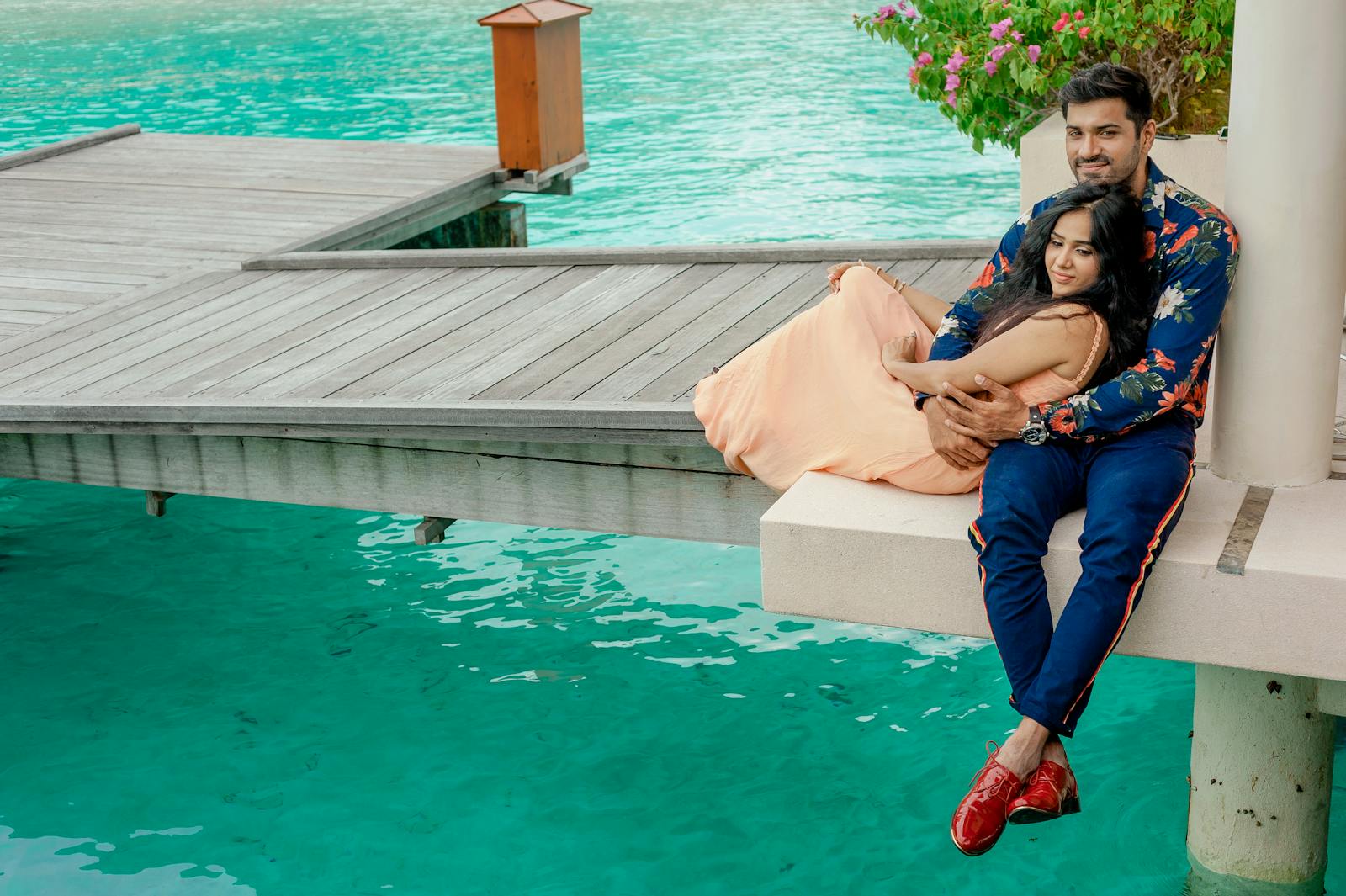 Couple embracing by a serene Maldives pier, capturing romance and tropical getaway vibes.