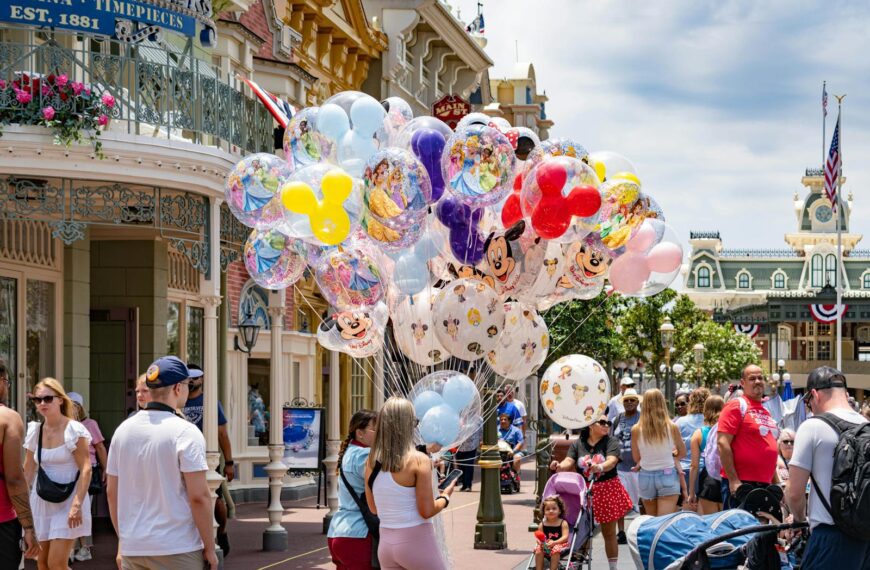 Colorful Disney-themed balloons on Main Street, USA at Disney World, with a lively crowd enjoying a sunny day.