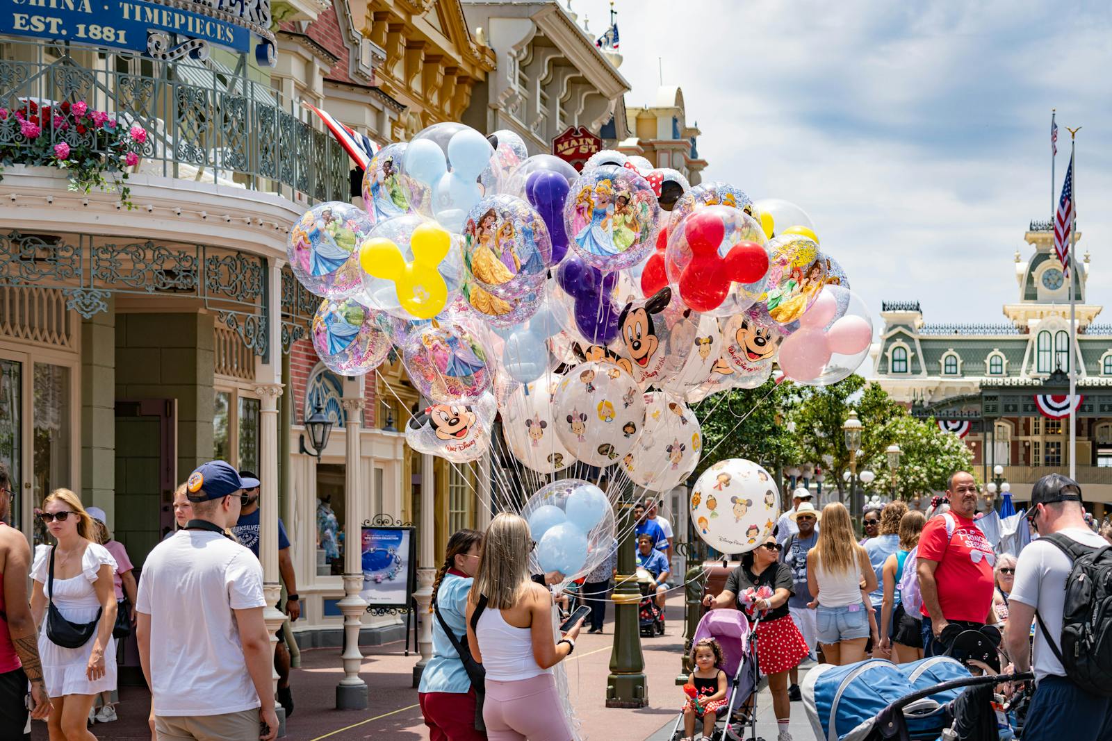 Colorful Disney-themed balloons on Main Street, USA at Disney World, with a lively crowd enjoying a sunny day.