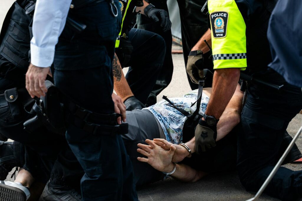 Multiple police officers detain a person on a city street, using handcuffs to restrain them.