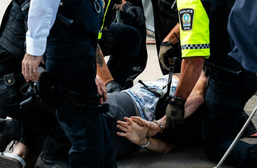 Multiple police officers detain a person on a city street, using handcuffs to restrain them.