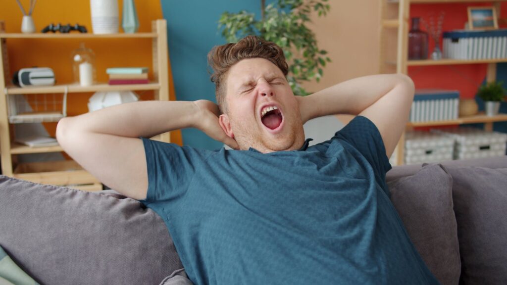 A man yawns while relaxing on a cozy couch in a modern living room.
