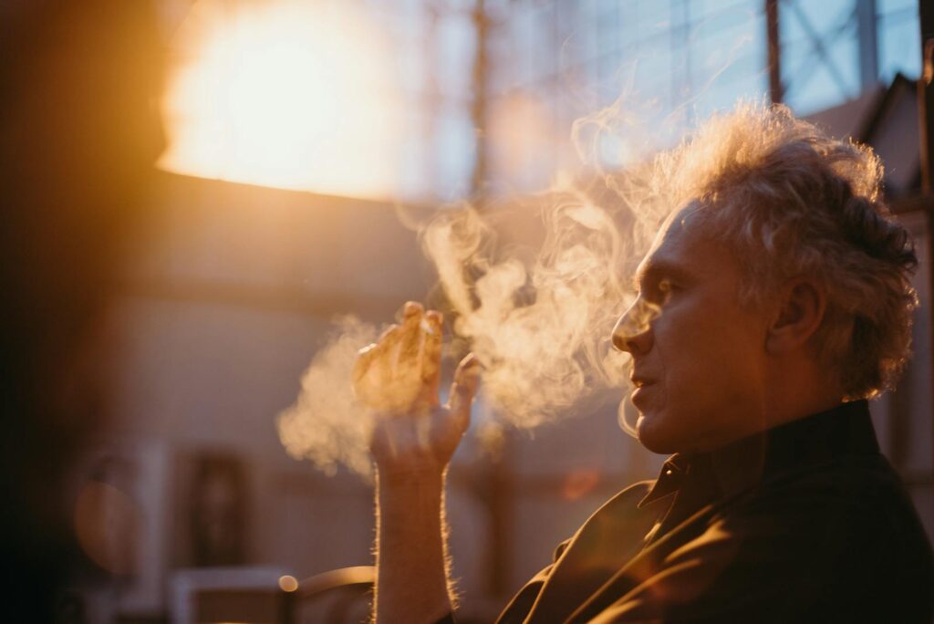 A senior man smoking in a room filled with warm, soft golden sunset light, deep in thought.