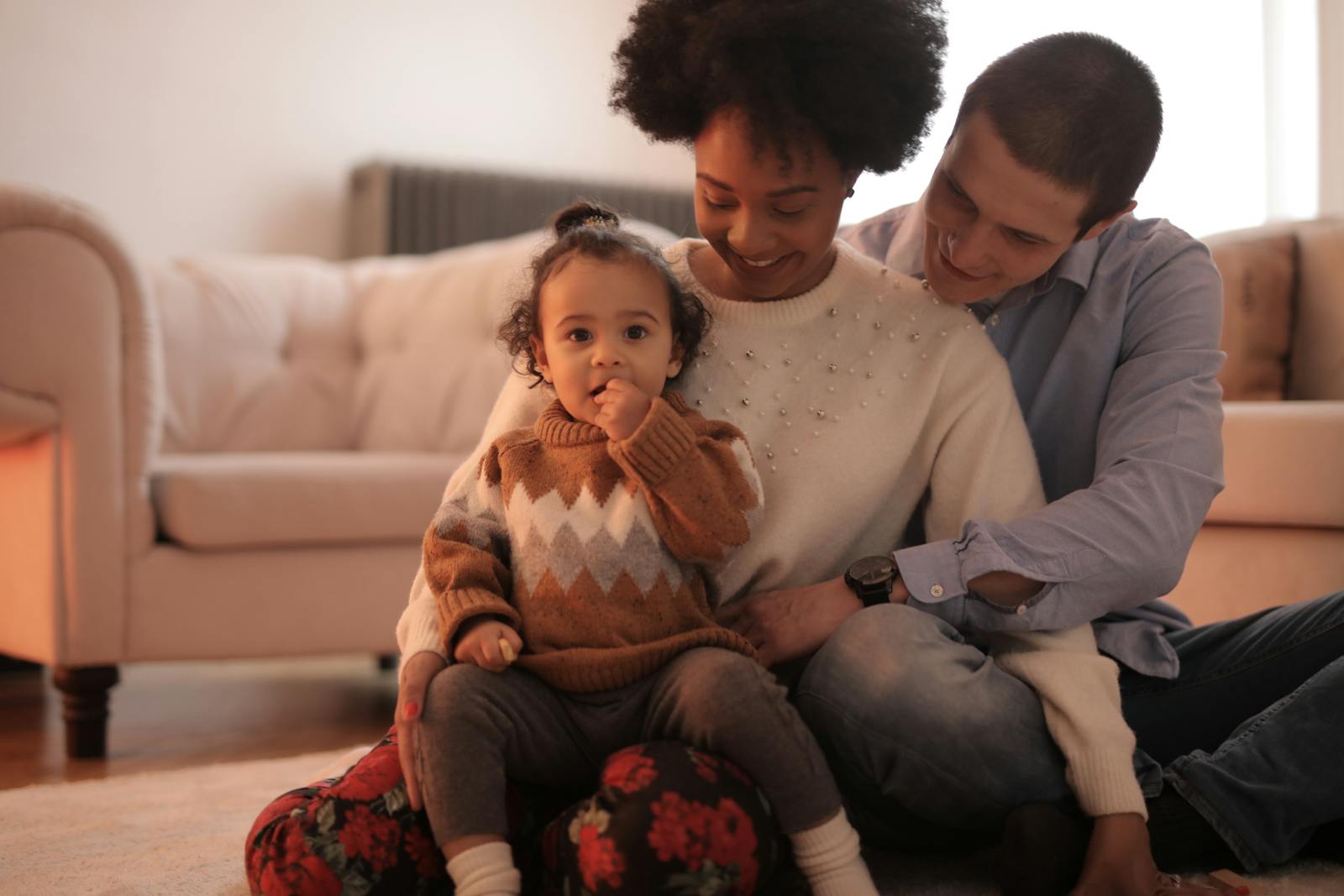 A joyful family moment with parents and child sitting on the floor in a cozy living room.