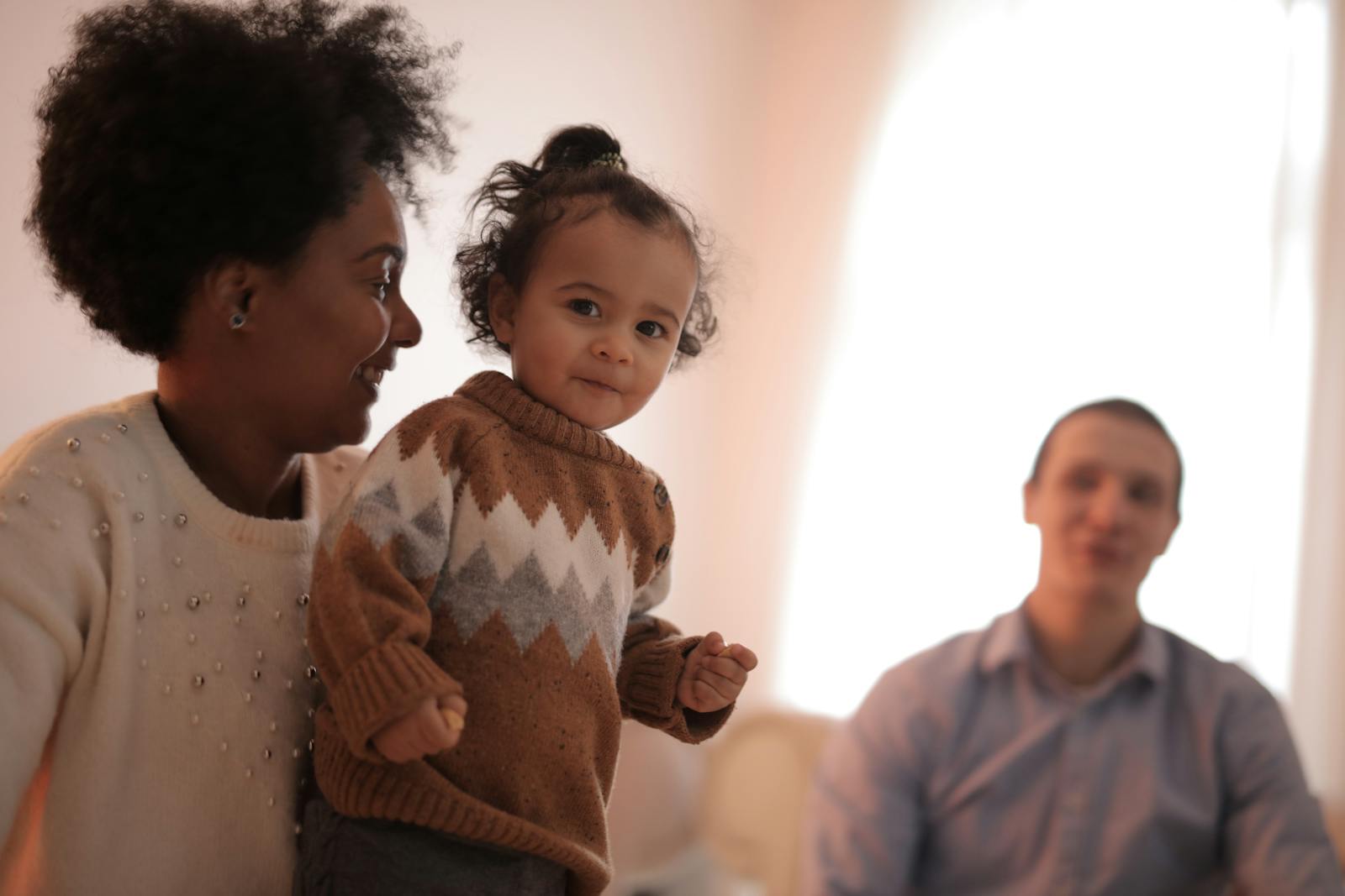 A joyful family moment indoors with a toddler smiling in a warm setting.