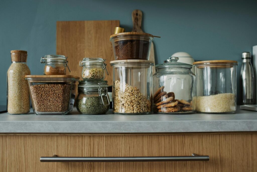 Glass jars with pantry essentials like oats, cookies, and spices on a kitchen counter.