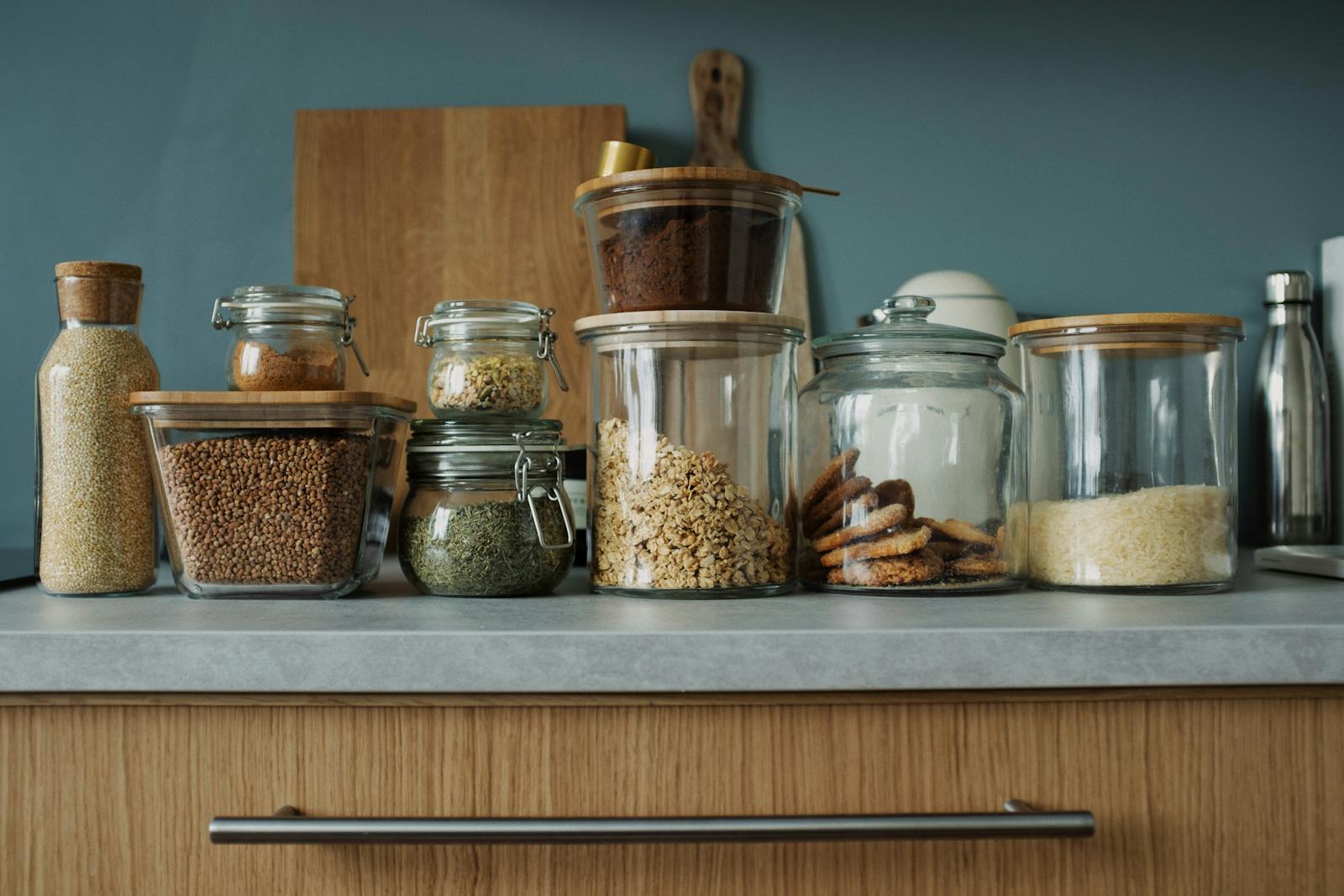 Glass jars with pantry essentials like oats, cookies, and spices on a kitchen counter.