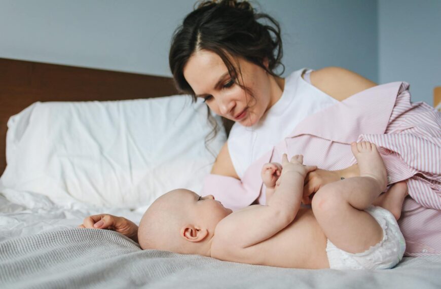 A mother lovingly interacts with her infant while lying on a bed.