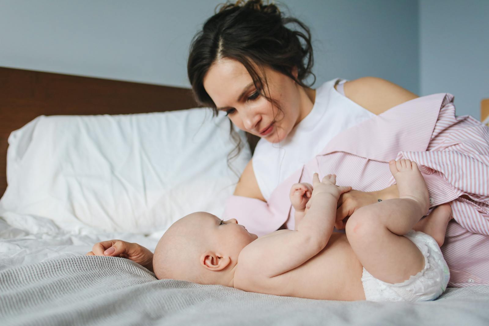 A mother lovingly interacts with her infant while lying on a bed.