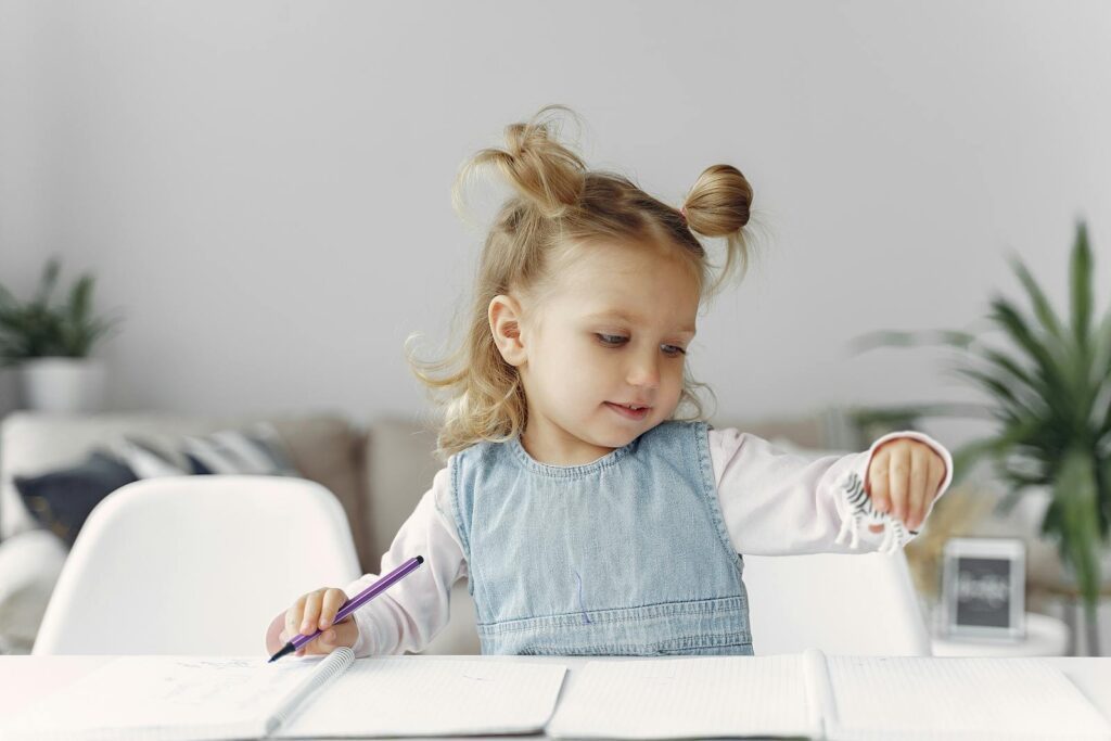Young girl engaged in playful and creative learning with a toy and notebook indoors.