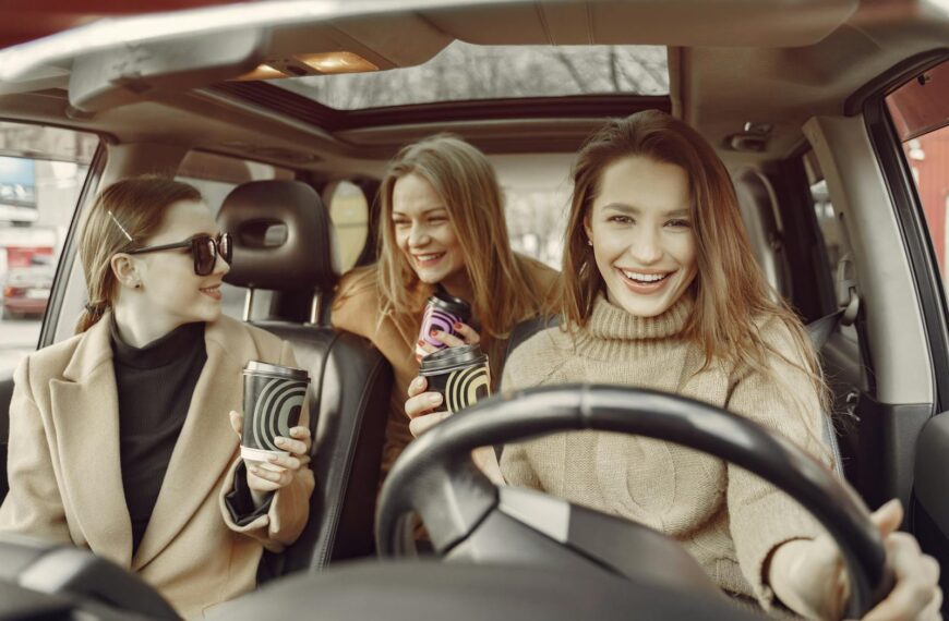 Happy friends relaxing with takeaway coffee in a car, sharing laughter and enjoyment on a casual day out.