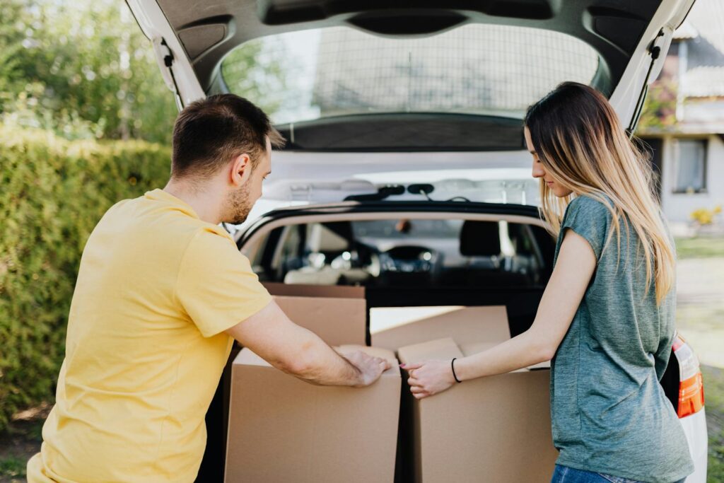 A couple loading cardboard boxes into a car trunk for moving day.