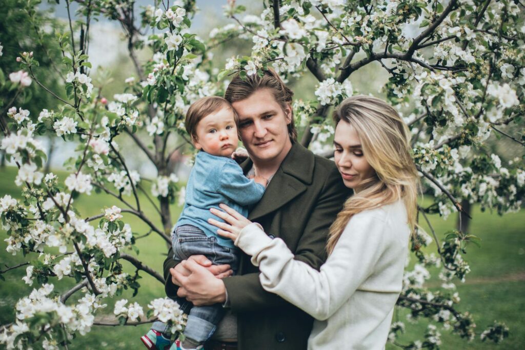 A family enjoying a loving moment together under a blossoming tree in the park during spring.