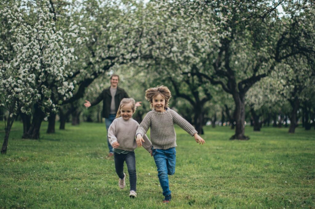 A cheerful father and two children running through a blossoming park, enjoying springtime together.