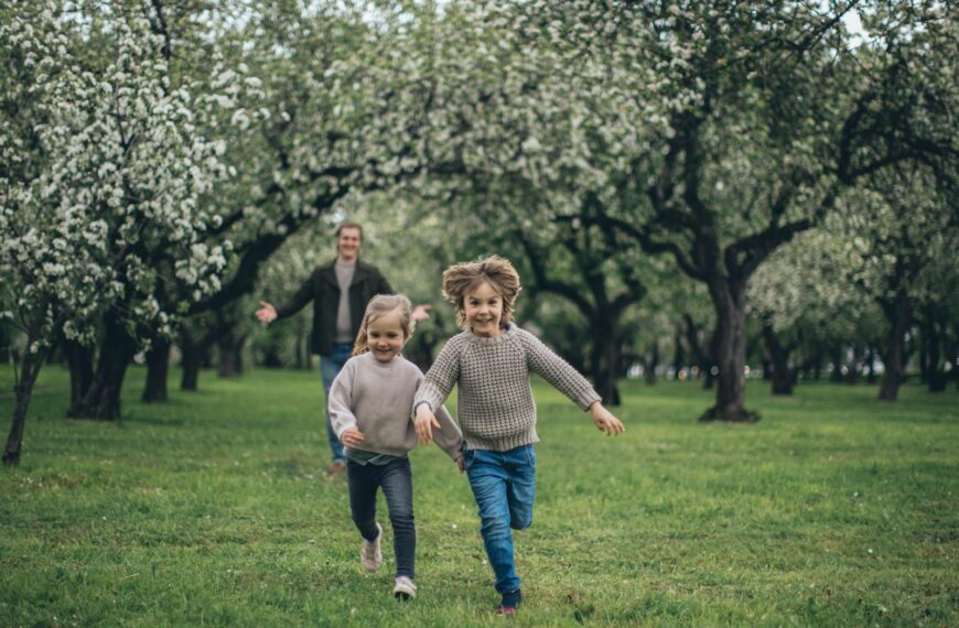 A cheerful father and two children running through a blossoming park, enjoying springtime together.