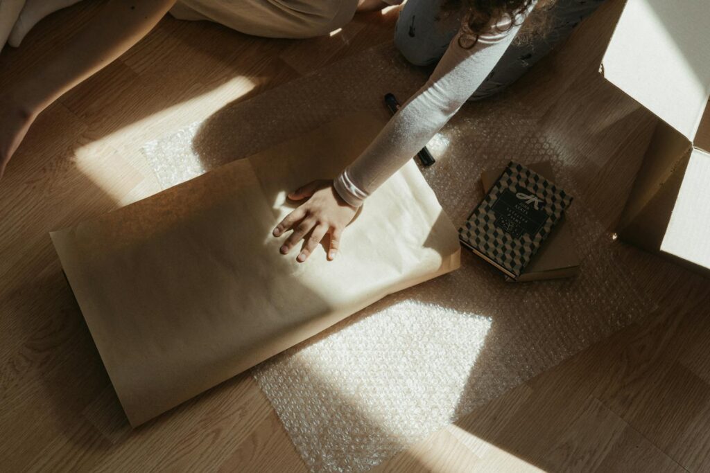 Person packing items on the floor using bubble wrap and packing paper.