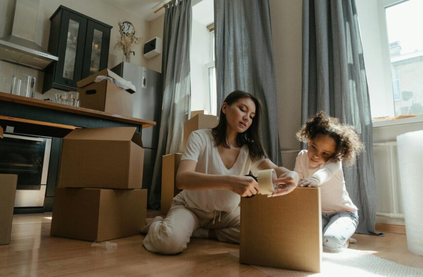 A mother and daughter pack boxes together in a sunny kitchen during a home move.