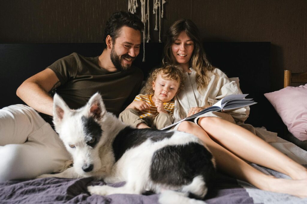 Happy family enjoying bonding time with child and pet, reading together on bed.