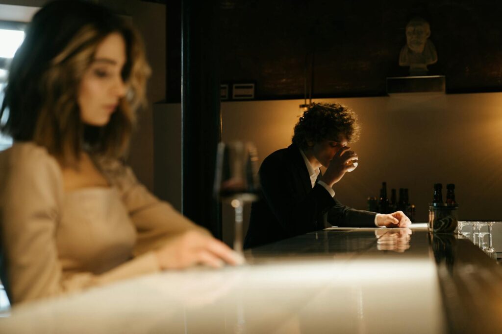A woman with curly hair and a man enjoying drinks at an elegant bar setting.