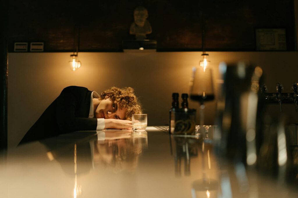 A thoughtful man in an elegant suit rests at a dimly lit bar counter, reflecting pensively.