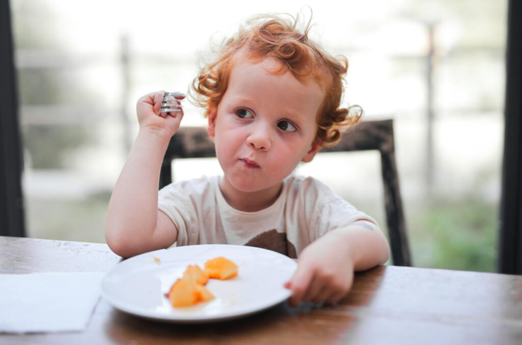 Adorable child enjoying a meal at a wooden table, highlighting childhood and innocence.