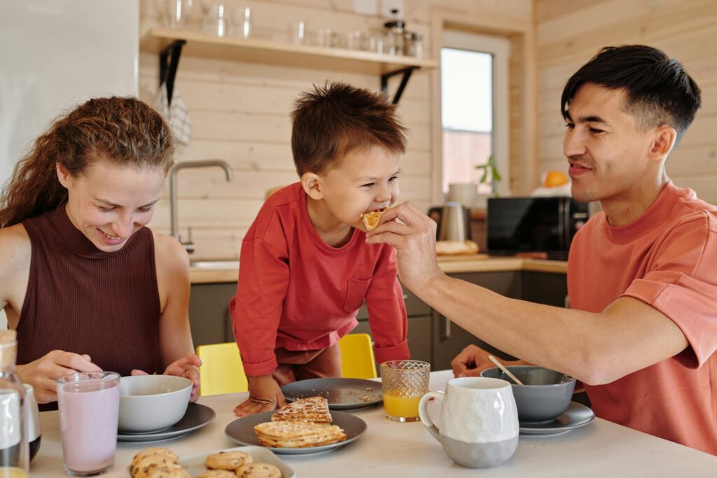 A joyful family of three shares breakfast in a cozy kitchen setting, depicting warmth and togetherness.