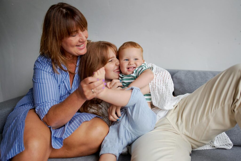 Happy grandmother with daughter and little boy resting on cozy couch in living room