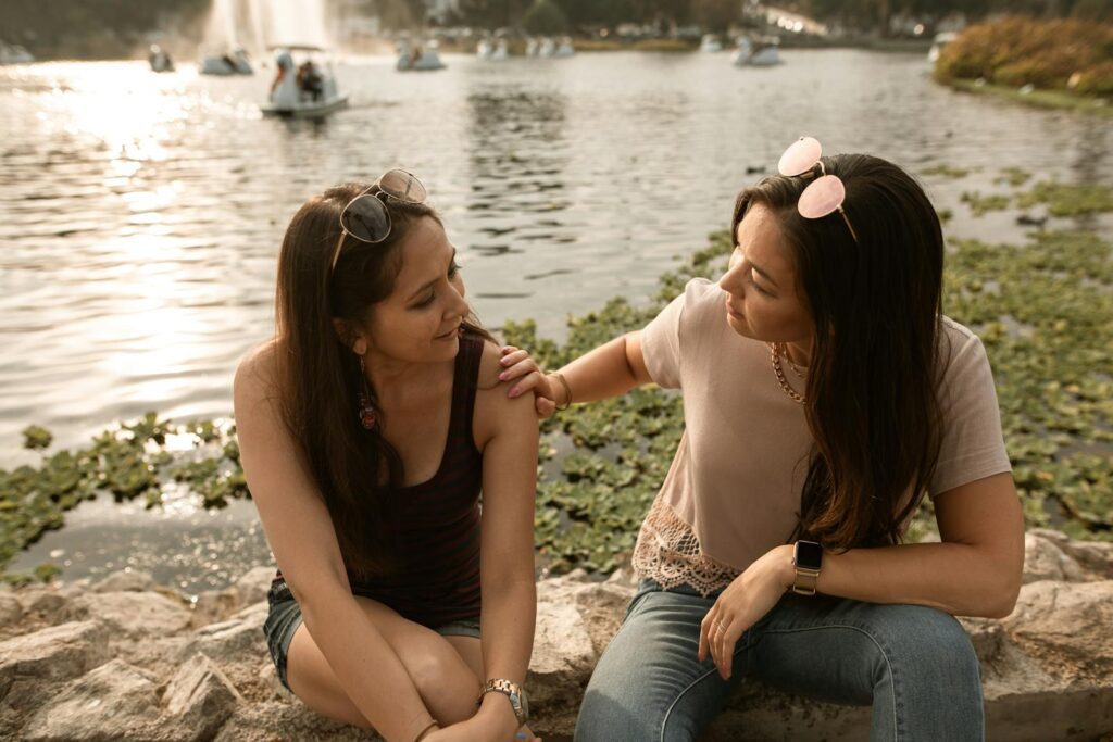 Two women having a heart-to-heart conversation by a sunny lakeside.